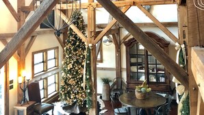 A rustic interior with exposed wooden beams, a wooden dining table, and a Christmas tree. - Designer Barnhouse located just 8 minutes from Main St on Private Gated Ranch (Fredericksburg)