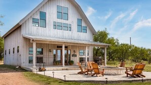 A large, single-story building with a prominent gable roof and a covered porch with outdoor seating. - Designer Barnhouse located just 8 minutes from Main St on Private Gated Ranch (Fredericksburg)