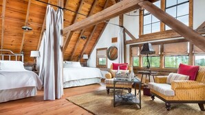 A high-ceilinged room with wooden beams, a bed, two sofas, a small table, and a window with a view. - Designer Barnhouse located just 8 minutes from Main St on Private Gated Ranch (Fredericksburg)