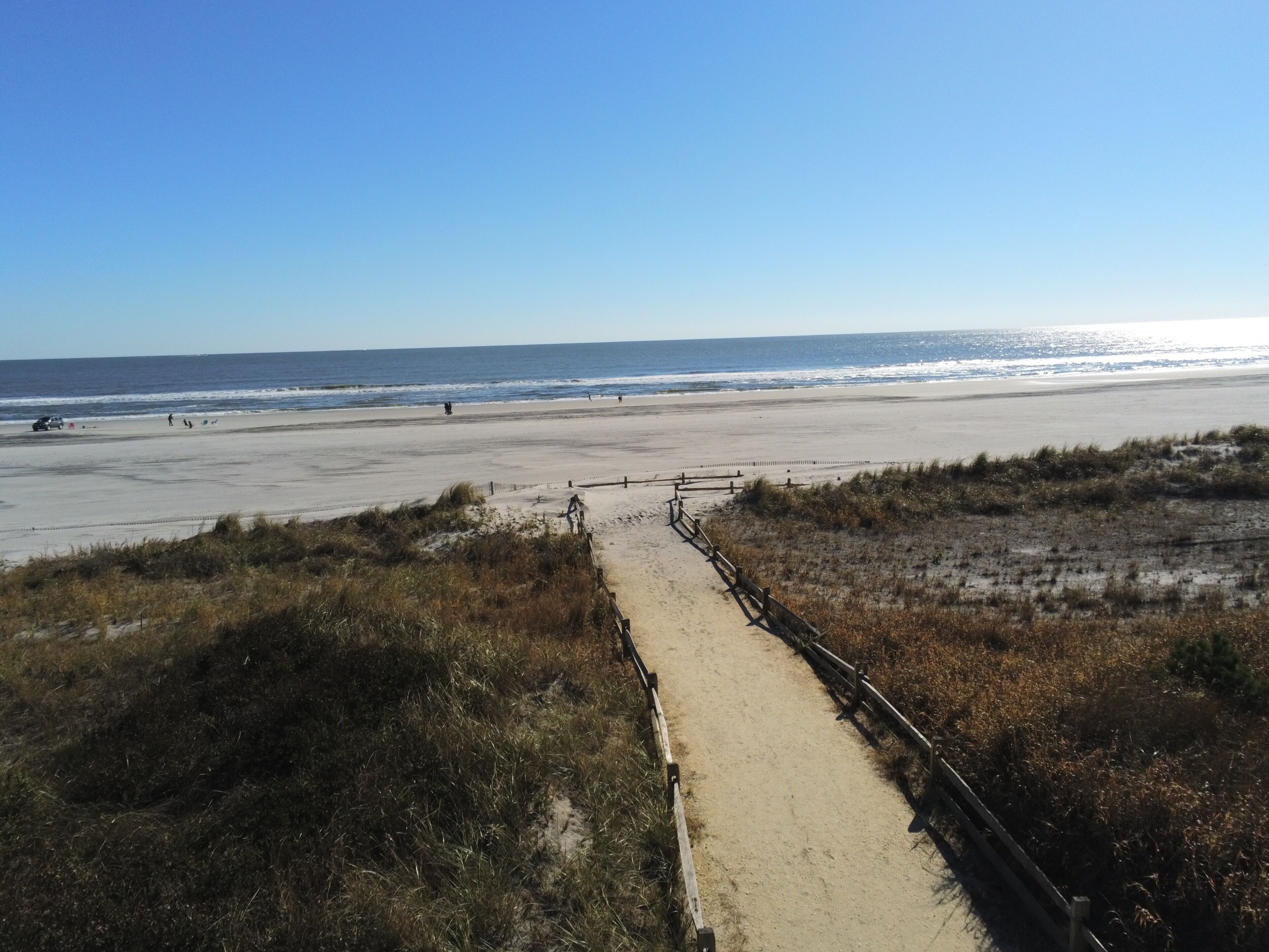 A beach pathway leading to the ocean with a clear sky.