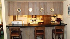 Een keuken met houten kastjes, een zwart aanrecht en drie barkrukken.