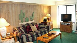 Een woonkamer met een houten wand, een bank, een bijzettafeltje, een televisie en een kast.