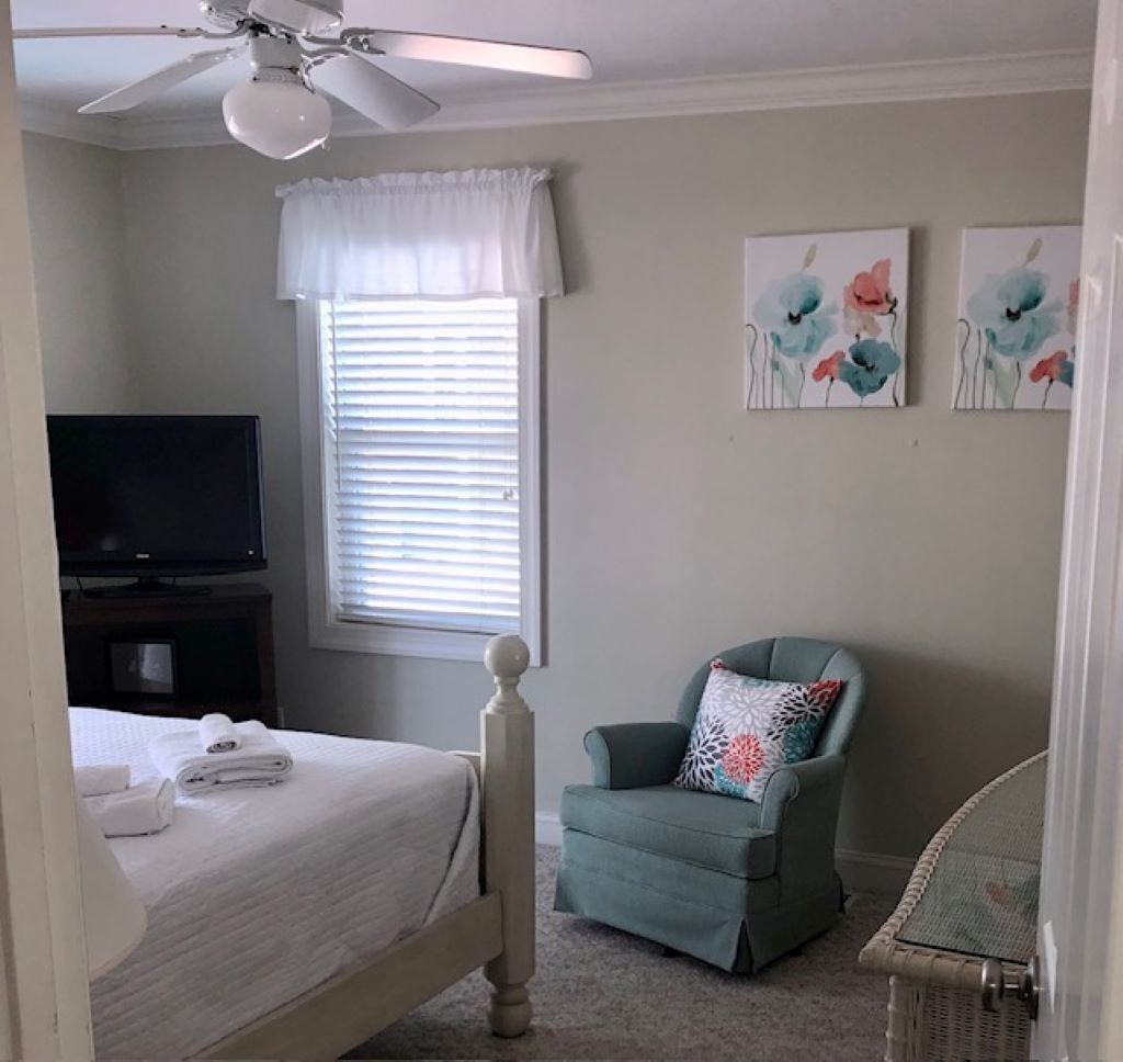 Un dormitorio con una cama, una silla, un televisor y una obra de arte en la pared.