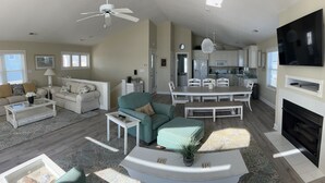 A spacious living room with a sofa, coffee table, and a dining area with chairs and a table. - Fabulous beach view!  Large pool…across from beach access. Decks on both levels! (Holden Beach)