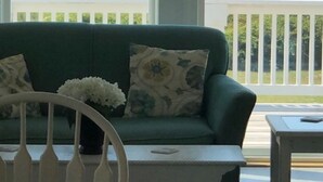 A room with a view of the beach, a green sofa, and a small table. - Fabulous beach view!  Large pool…across from beach access. Decks on both levels! (Holden Beach)