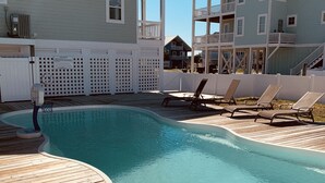 A swimming pool with a wooden deck, lounge chairs, and a white fence with pool rules posted. - Fabulous beach view!  Large pool…across from beach access. Decks on both levels! (Holden Beach)