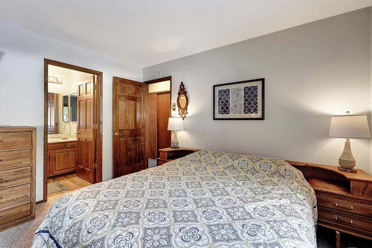 Une chambre à coucher avec une couvre-lit à motifs, une armoire en bois et une table de chevet avec une lampe.