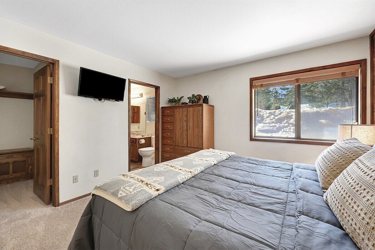 A bedroom with a bed, a wardrobe, a television, and a window with a view of trees.