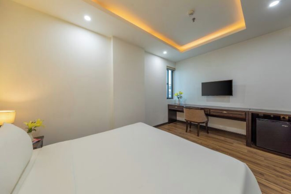 A hotel room with a bed, a desk, a chair, a TV, and a small kitchenette.