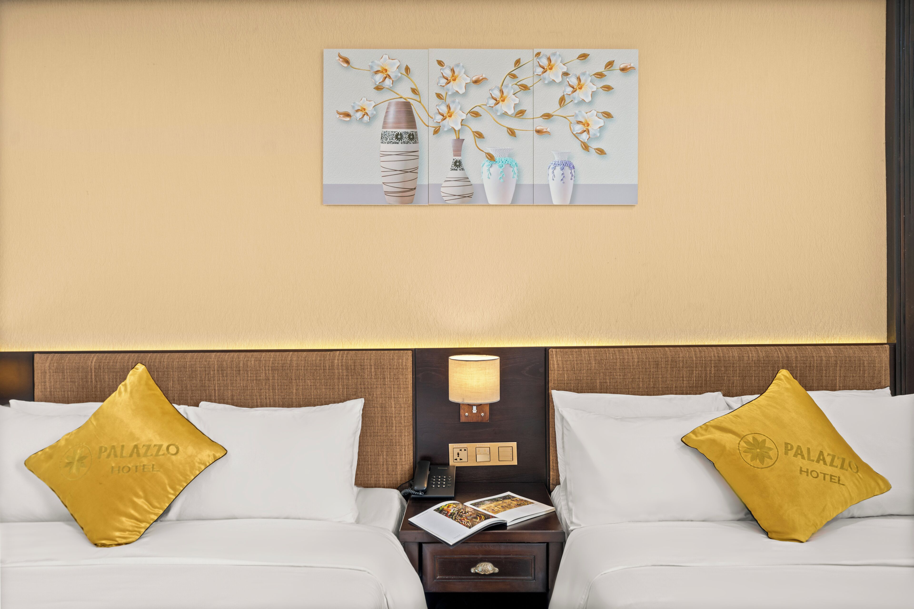 Habitació d'hotel amb dos llits, una tauleta de nit amb una làmpada i una obra d'art penjada a la paret.