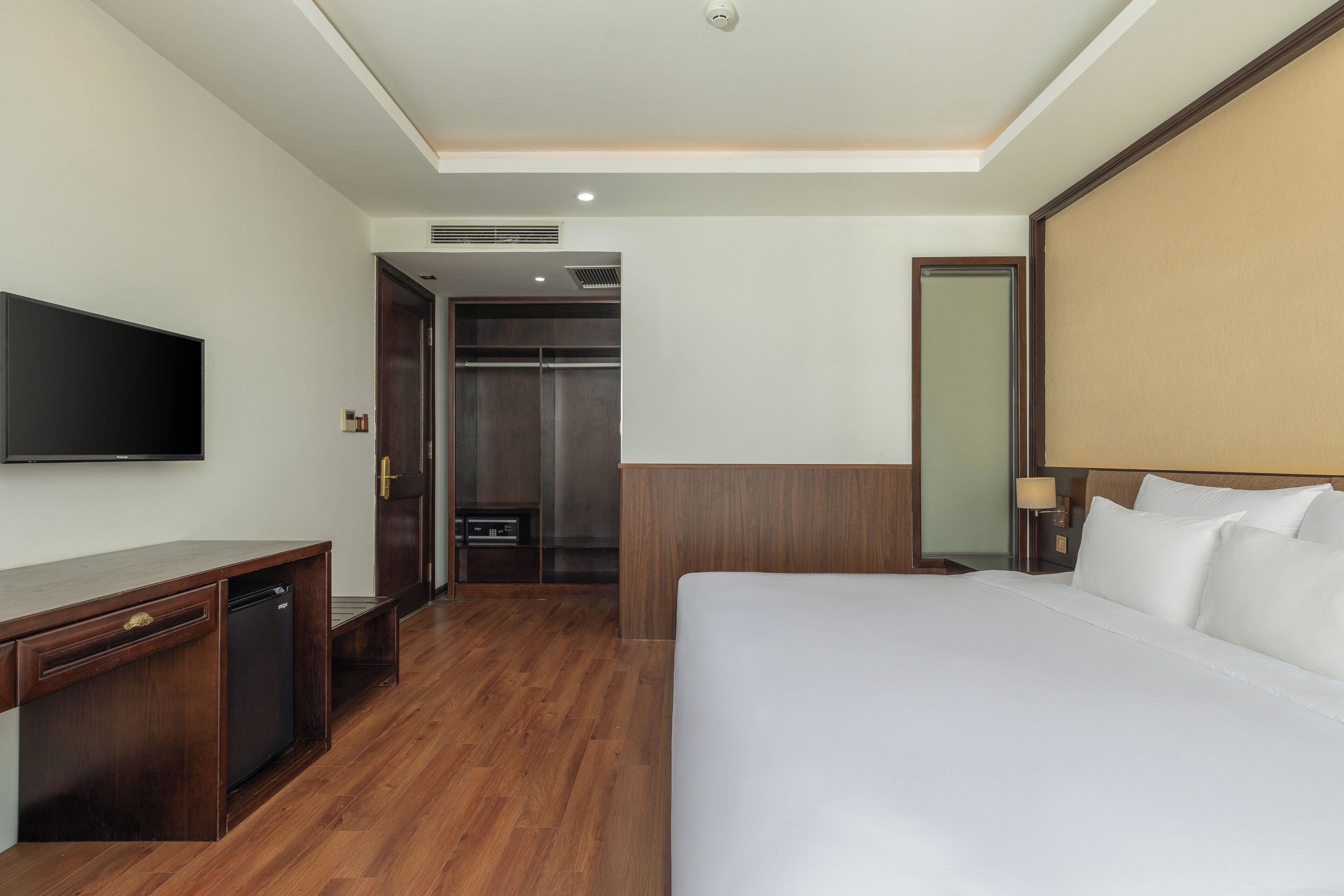 A hotel room with a bed, a desk, a television, a wardrobe, and a mirror.