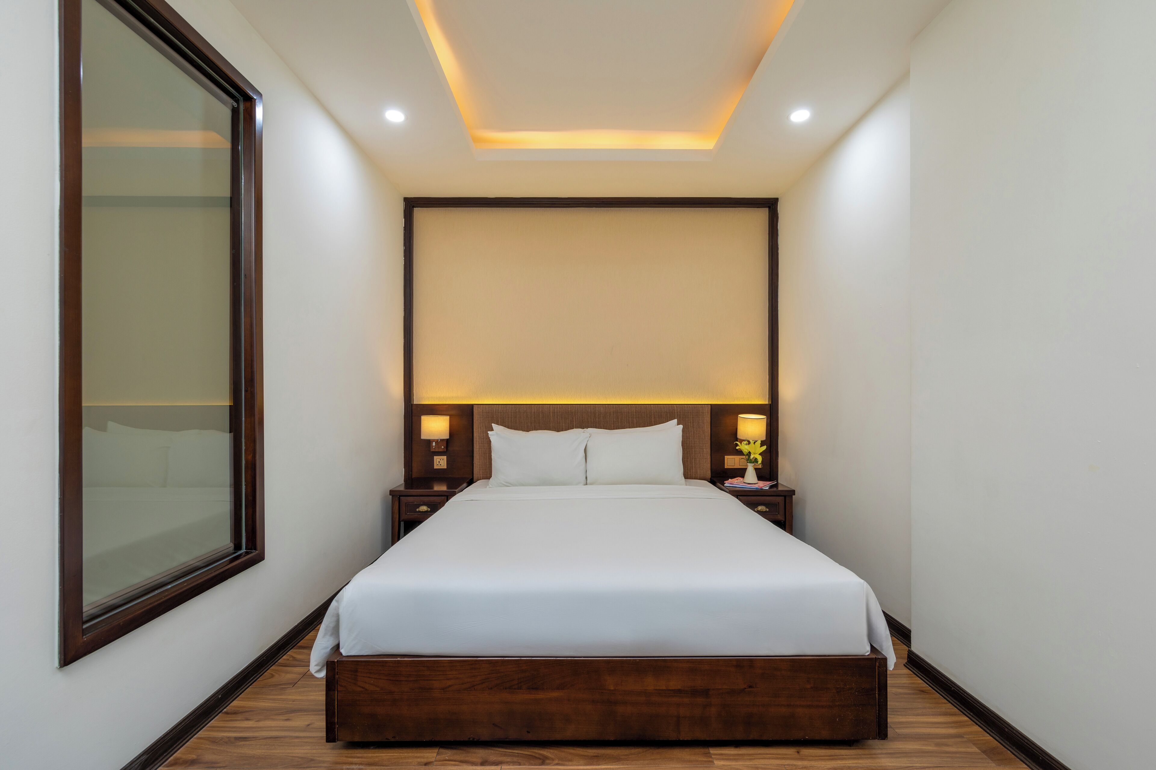 A modern hotel room with a large bed, wooden headboard, bedside lamps, and a large window.