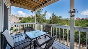 A covered outdoor patio with a table and chairs, surrounded by a wooden railing and a view of houses and trees. - Come and enjoy our large intercoastal beach suite with pool (Indian Shores)