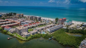 An aerial view of a coastal resort area with multiple buildings, a beach, and a water body. - Come and enjoy our large intercoastal beach suite with pool (Indian Shores)
