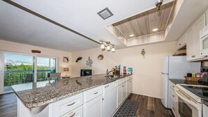 A modern kitchen with white cabinets, granite countertops, and a large island. There is a view of the outdoors through a sliding glass door. - Come and enjoy our large intercoastal beach suite with pool (Indian Shores)