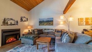Una sala de estar acogedora con chimenea, un sofá modular, una mesa de centro y decoración en la pared.