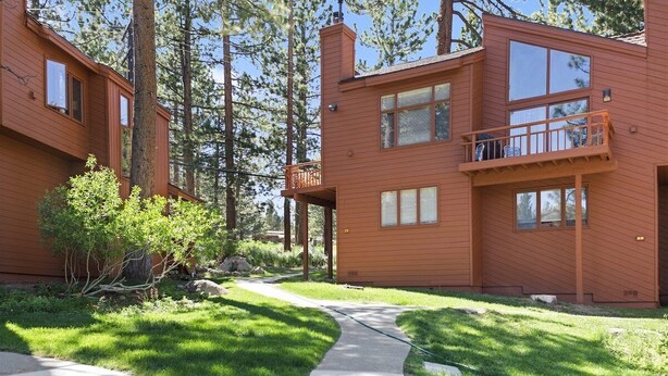 A two-story wooden cabin with a balcony, surrounded by a well-maintained lawn and tall trees. - Woodlands 28: Pet Friendly, On Sierra Star Golf Co (Mammoth Lakes)