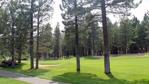 A golf course with a well-maintained green, a paved path, and tall pine trees. - Woodlands 28: Pet Friendly, On Sierra Star Golf Co (Mammoth Lakes)