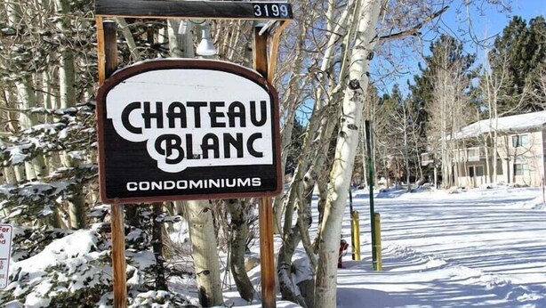 A sign for Chateau Blanc Condominiums with a stone base and wooden posts. - Chateau Blanc 30: One car garage, near town (Mammoth Lakes)