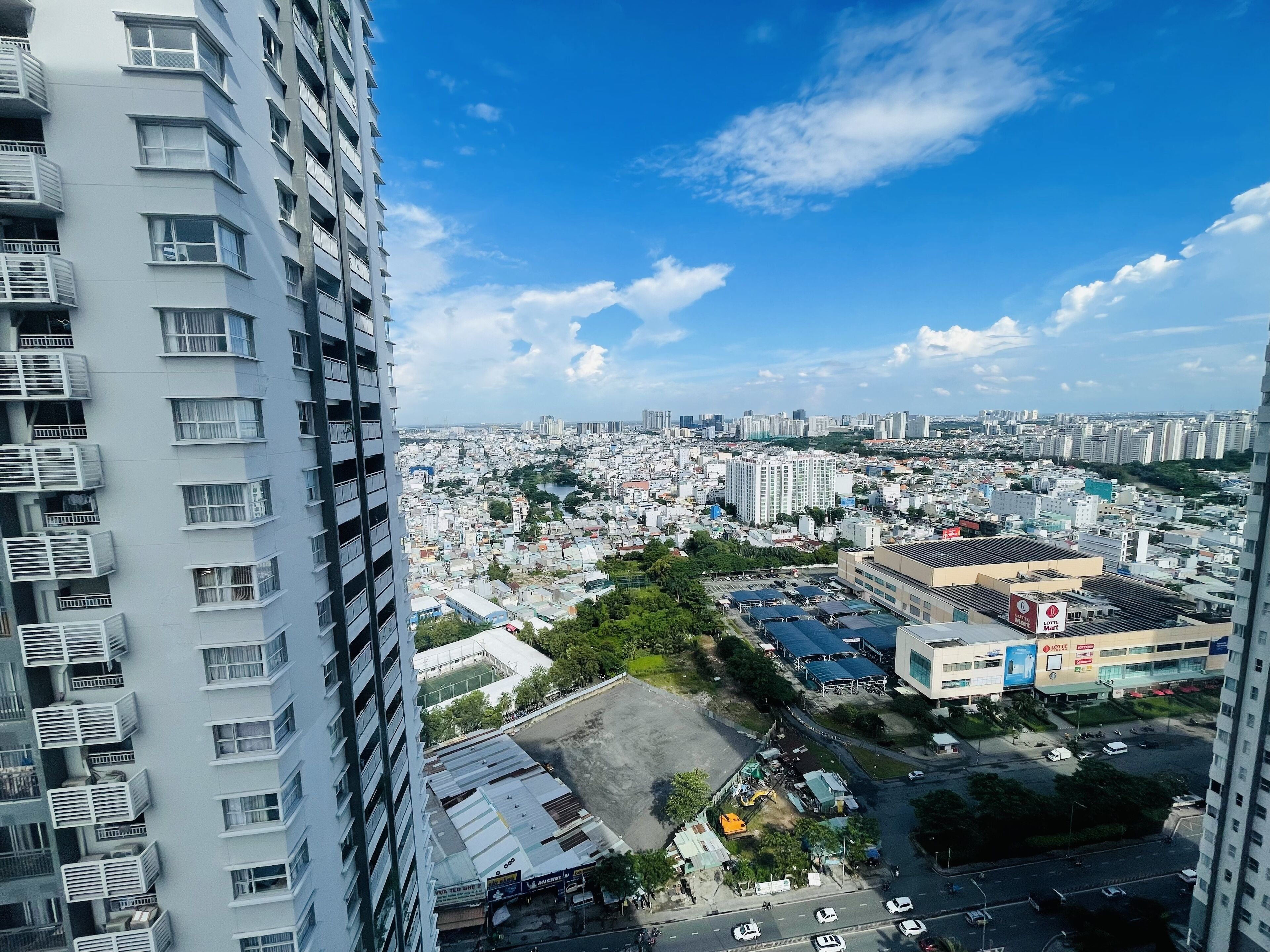 A high-rise building with multiple balconies and a view of a cityscape with various buildings and a river.