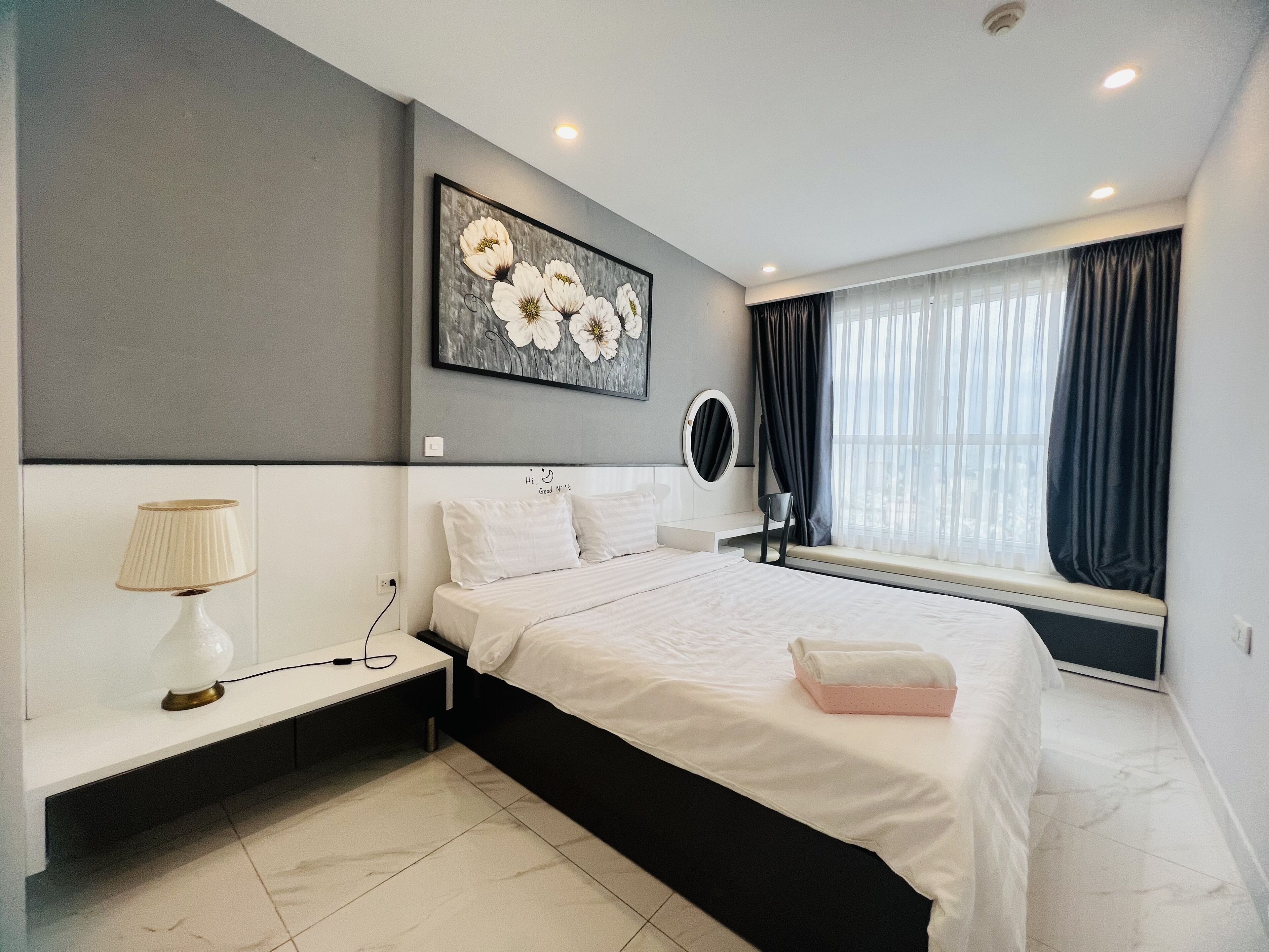 A modern bedroom with a bed, bedside table, lamp, and a large window with curtains.