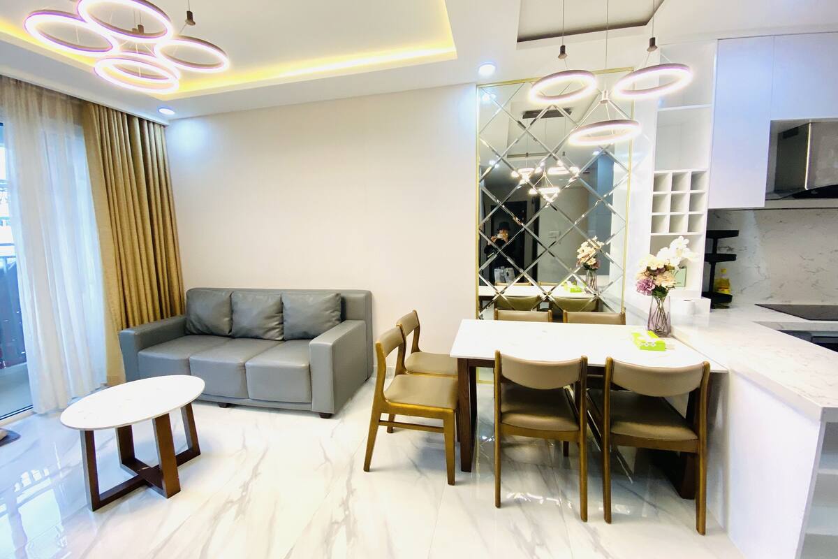 Ein modernes Wohnzimmer mit grauem Sofa, einem Esstisch mit vier Stühlen und einer Küchenzeile mit Edelstahl-Dunstabzugshaube.