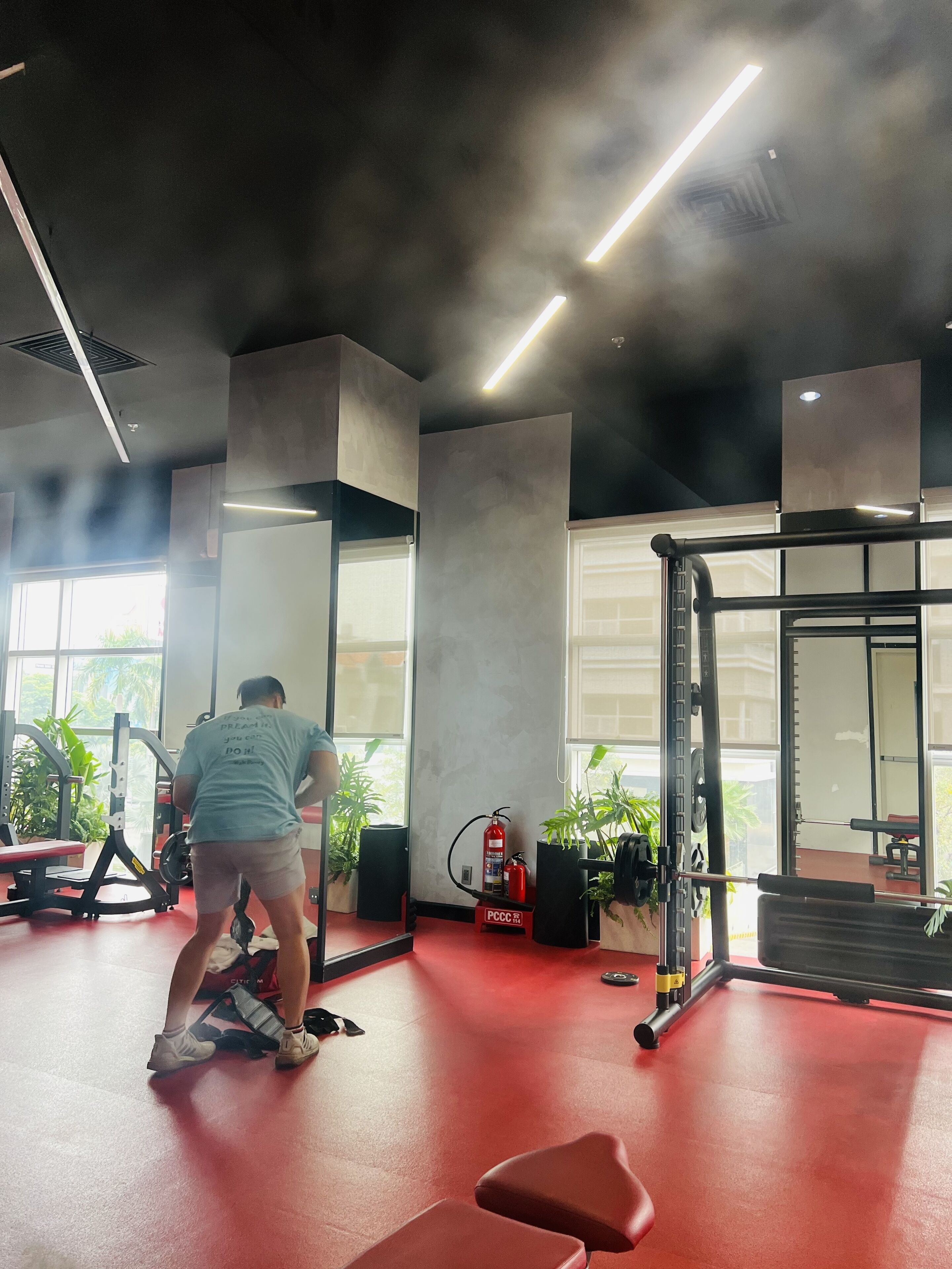 Un gimnasio con equipamiento de ejercicio, un extintor y plantas en macetas.