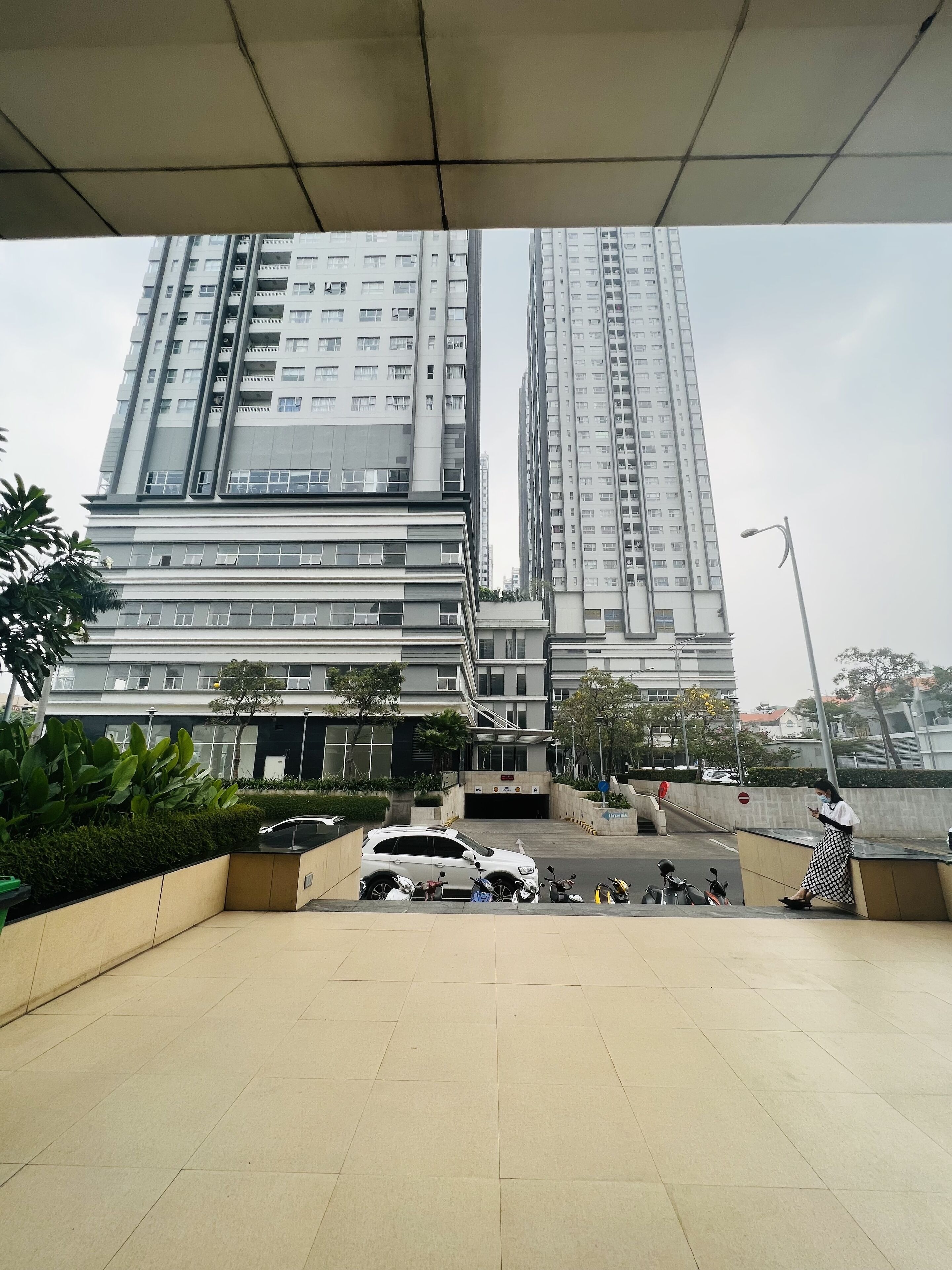 A modern building with multiple floors, a parking area with several cars, and a few motorcycles.