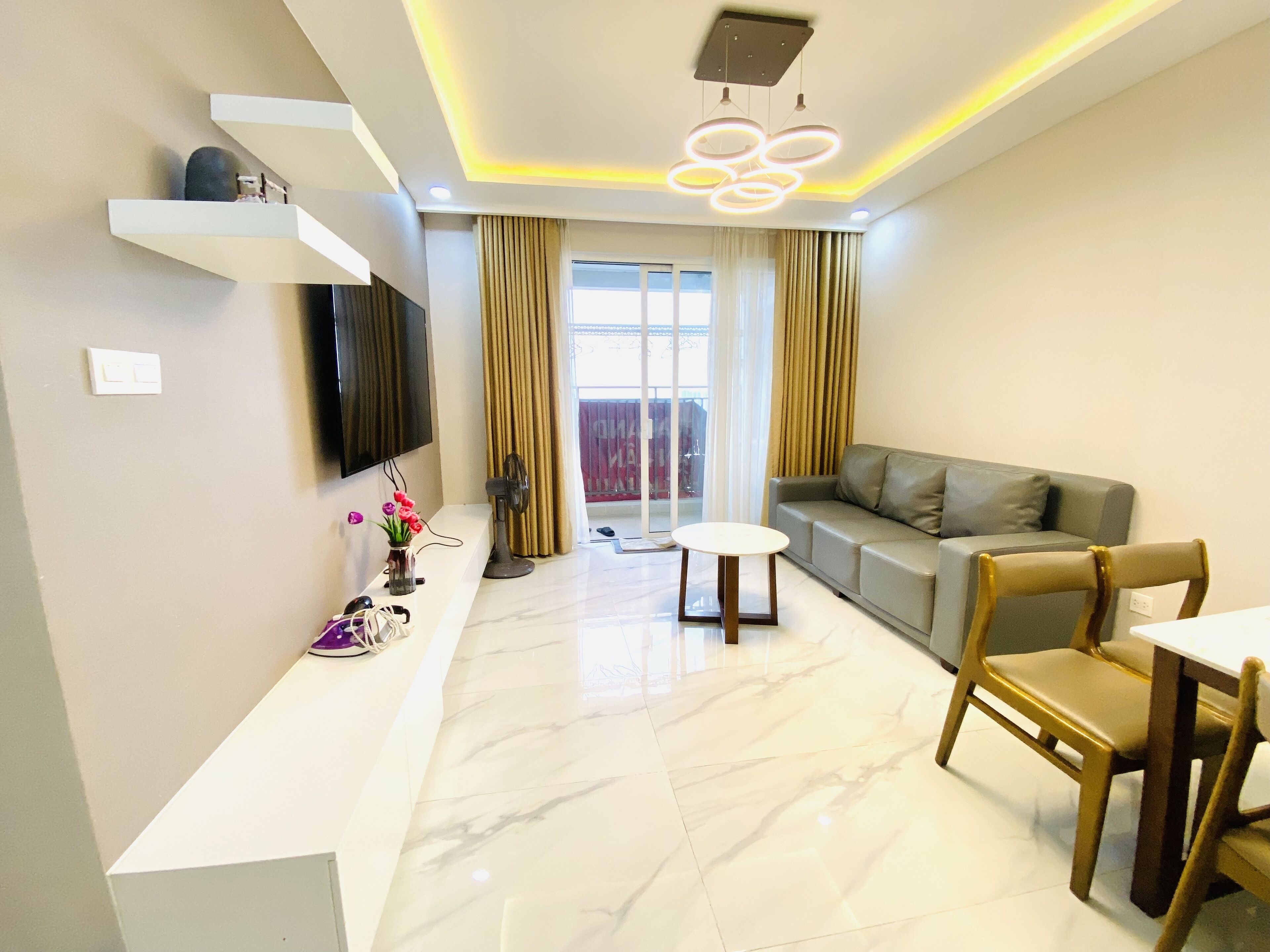 A modern living room with a sofa, a dining table, and a TV mounted on the wall.