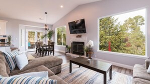 A spacious living room with a fireplace, a television mounted on the wall, and large windows offering a view of the outdoors. - Fabulous 4 Bed/3 Bath Rental on Lodge Hill! Updated, Charming & Pet-Friendly! (Cambria)