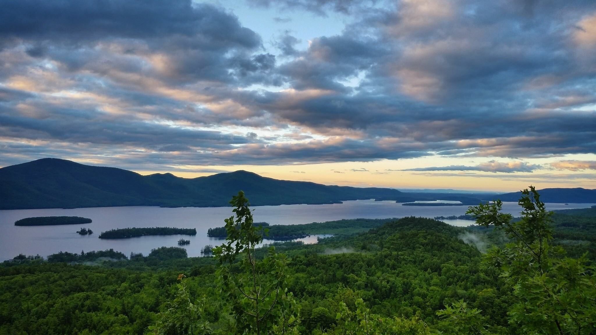 A panoramic view of a lake surrounded by mountains and dense forest.