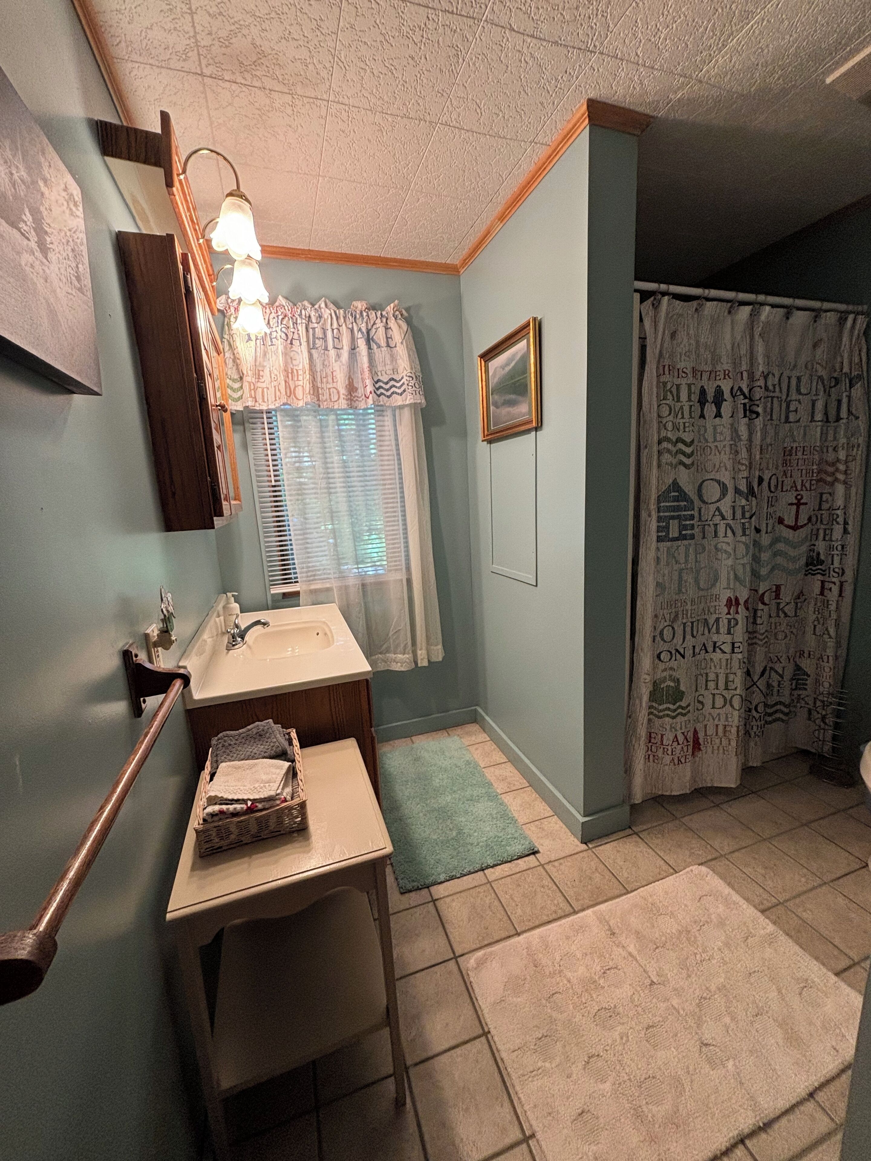 A bathroom with a sink, mirror, towel rack, and a window with blinds.