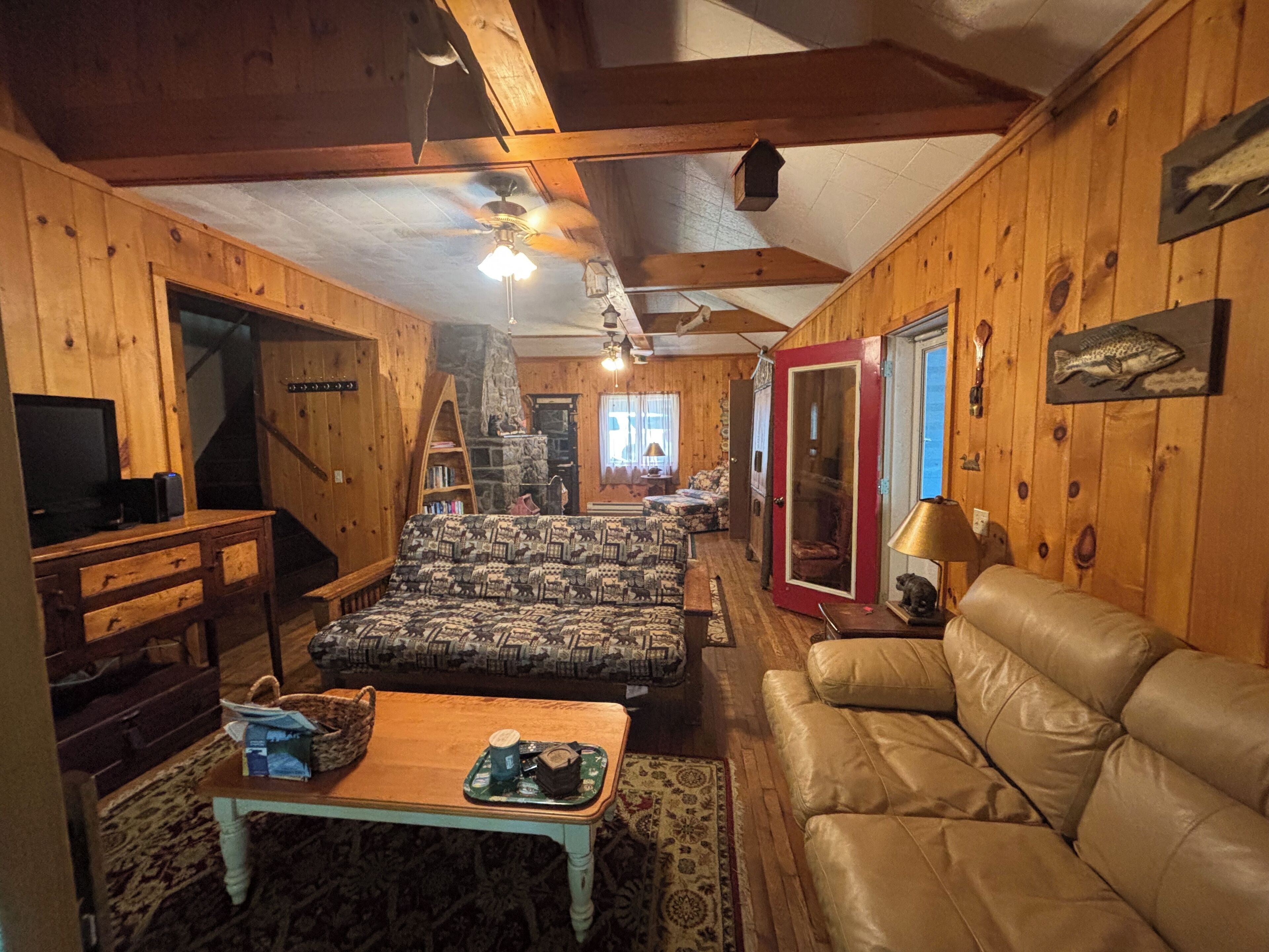 Interior acolhedor de uma cabana com decoração em madeira, um sofá, um estofado de couro, uma televisão e uma lareira.
