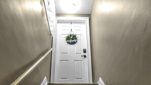 A wooden staircase with a white door at the top, a light fixture above, and a 'Welcome' sign on the wall. - Spacious/Comfy/Private Home near Buffalo/Bills/Airport/Niagara Falls (Depew)