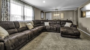 A living room with a large L-shaped sectional sofa, a dining table with chairs, and a chandelier. - Spacious/Comfy/Private Home near Buffalo/Bills/Airport/Niagara Falls (Depew)