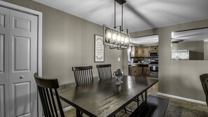 A dining area with a wooden table, four chairs, a chandelier, and a kitchen in the background. - Spacious/Comfy/Private Home near Buffalo/Bills/Airport/Niagara Falls (Depew)