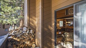 Facciata in legno con una pila di legna da ardere e una porta vetrata che dà su un interno con un divano e zona pranzo.