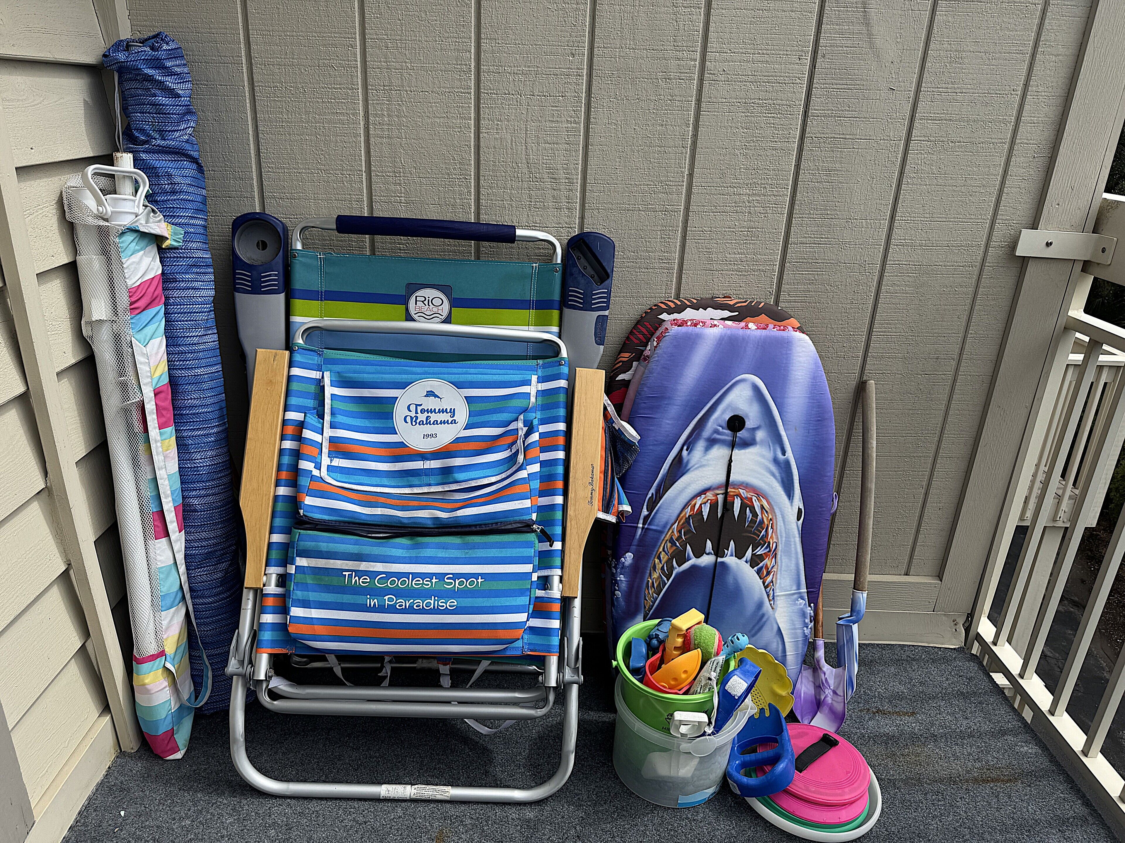 Una sedia da spiaggia con motivo squalo, una borsa da spiaggia a righe e un secchio pieno di giochi da spiaggia.
