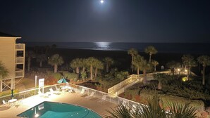 Vista nocturna de una piscina con vistas al océano, palmeras y un edificio con balcón.