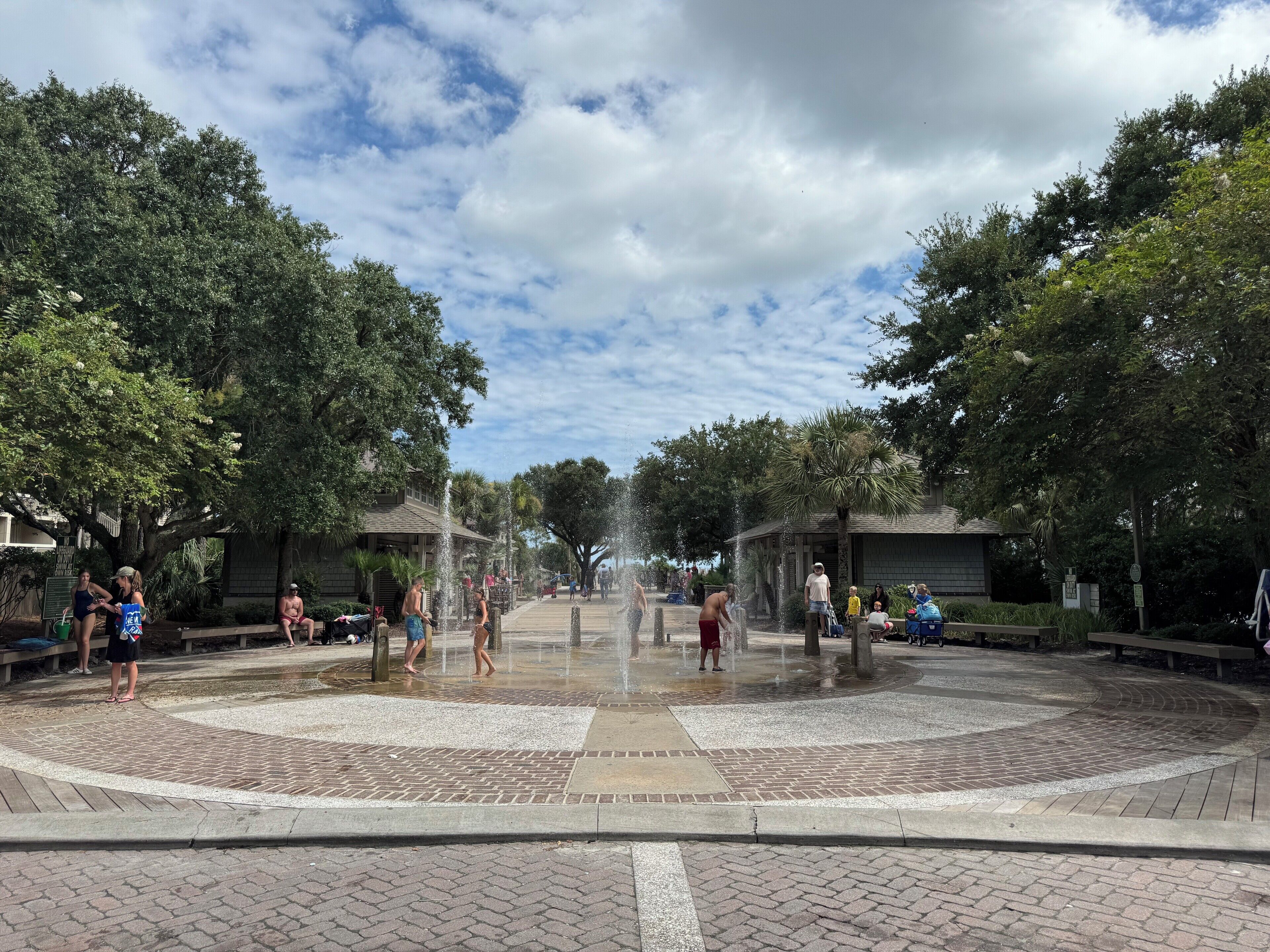 Una plaza pública con una fuente central, rodeada de  árboles y bancos.