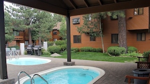 Un área de piscina al aire libre con techo, que incluye dos piscinas, una parrilla para barbacoa y un banco de madera.