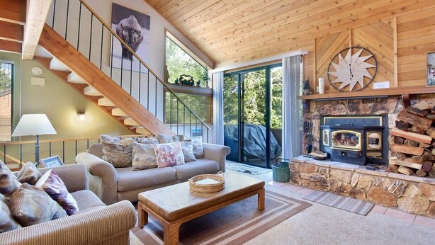 Un salón amplio con escalera de madera, chimenea y un ventanal grande.