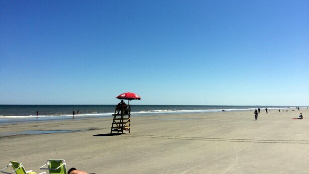 Een strand met een torenwachterspost en een rode parasol, omgeven door zand en de oceaan.