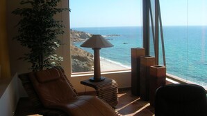 A room with a view of the ocean, a brown leather chair, a floor lamp, and a potted plant. - The Red House - Quiet, romantic weekend (Los Barriles)