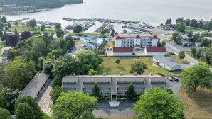 Luftaufnahme eines Küstenhafens mit einem großen Gebäude mit rotem Dach und zahlreichen Fenstern, umgeben von üppigem Grün und Liegeplätzen für Boote.