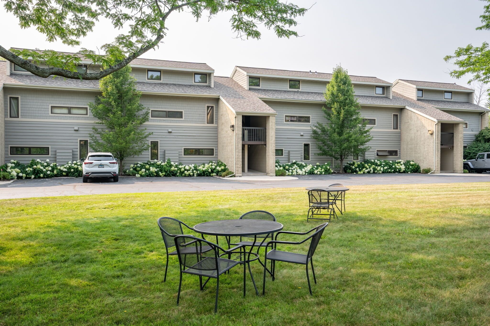 A multi-story residential building with a grassy lawn, outdoor seating area, and a car parked in front.
