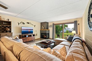 A spacious living room with a fireplace, a television, and a large window offering a view of the outdoors.