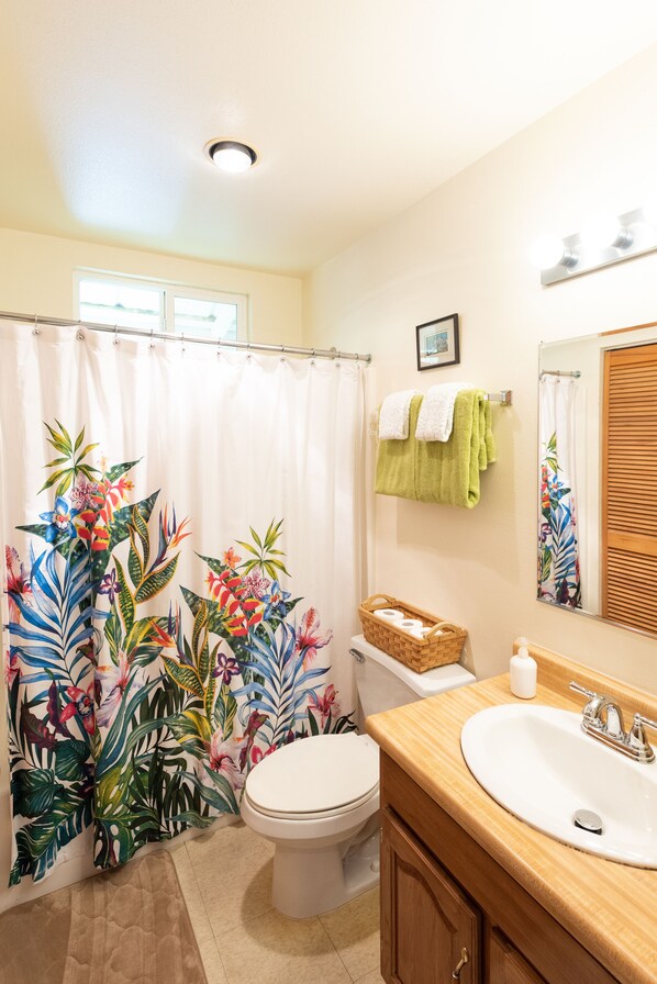 Un baño con inodoro, lavamanos y cortina de ducha con diseño tropical.