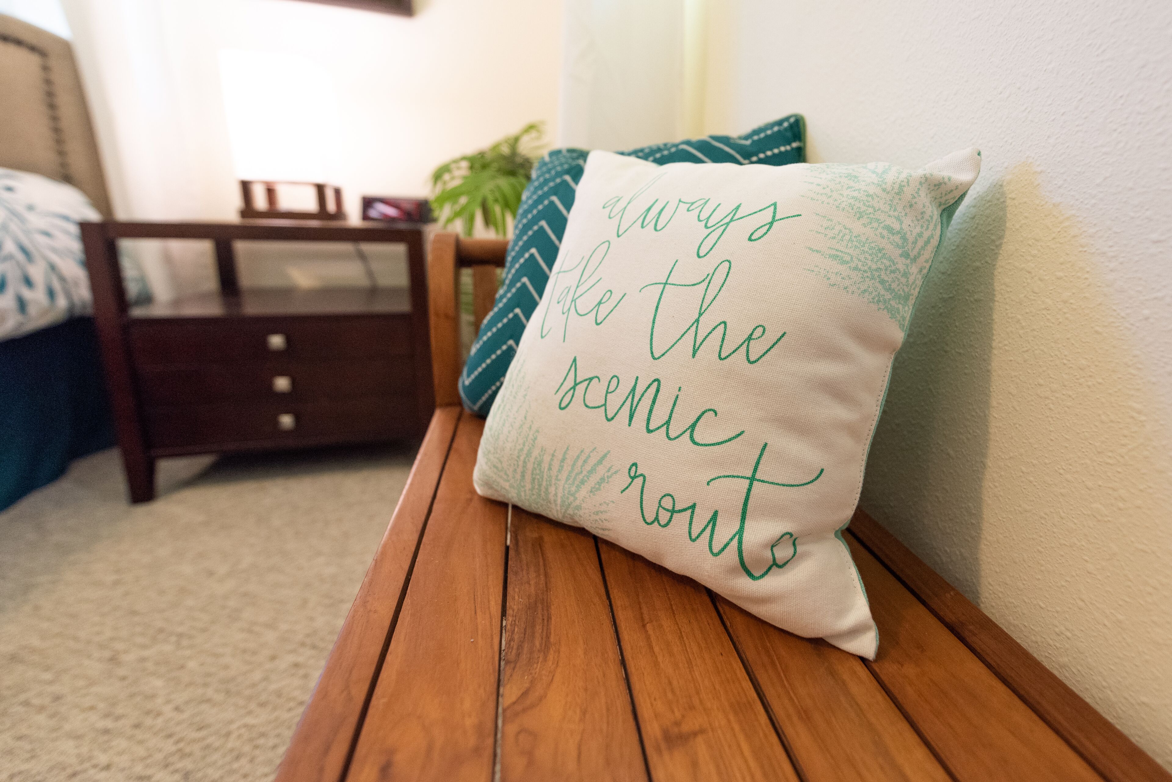 Un banc en bois avec un coussin sur lequel est brodé le message : « Empruntez toujours le chemin le plus pittoresque. »
