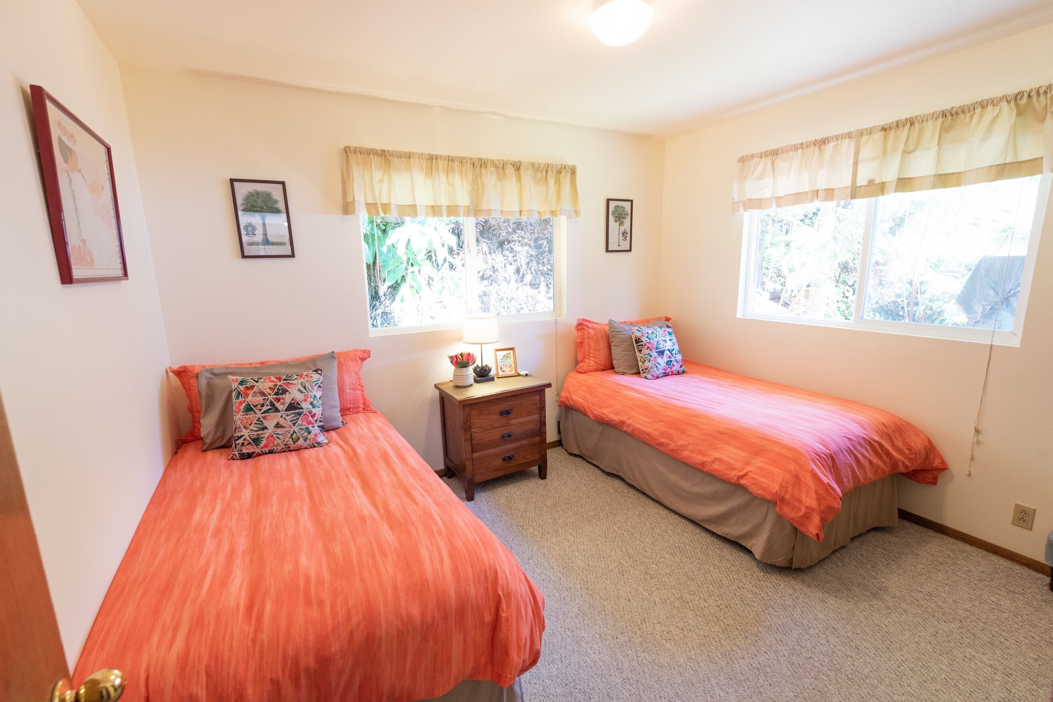 A bedroom with two beds, a nightstand, and two windows with curtains.